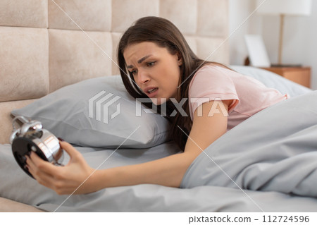 Frustrated woman waking to alarm clock noise Frustrated woman waking to alarm clock noise 112724596