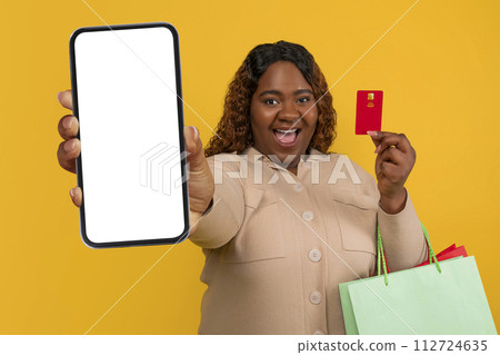 Happy young chubby black woman showing phone and credit card Happy young chubby black woman showing phone and credit card 112724635