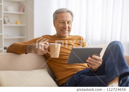 Happy elderly man drinking coffee and using digital tablet 112724656