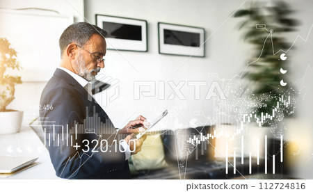 Mature businessman in a suit attentively examines his tablet, standing in a modern office Mature businessman in a suit attentively examines his tablet, standing in a modern office 112724816