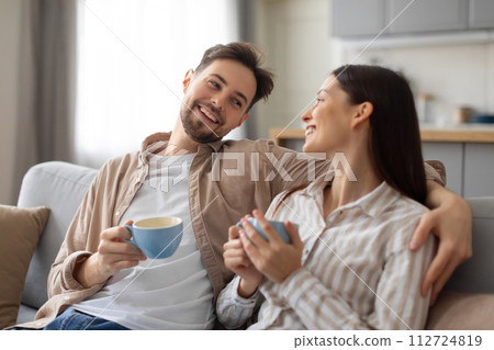 Happy european couple enjoying coffee on couch and chatting Happy european couple enjoying coffee on couch and chatting 112724819