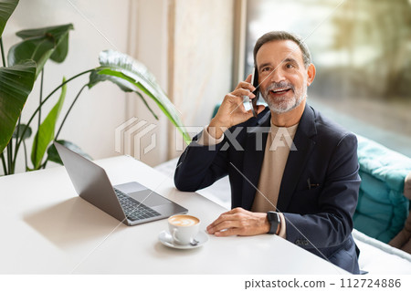 Engaged and happy mature businessman in a black blazer talking on a mobile phone 112724886