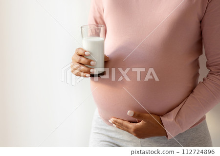 Pregnant woman cradling her belly and holding glass of milk 112724896