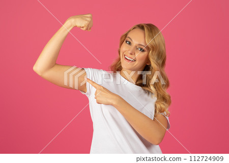 Cheerful blonde woman pointing at her biceps over pink background 112724909