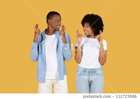 A joyful young couple in casual wear happily making the fingers crossed gesture 112725086