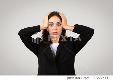 Stressed businesswoman with wide eyes and a worried expression, clutching her head in alarm or frustration Stressed businesswoman with wide eyes and a worried expression, clutching her head in alarm or frustration 112725118