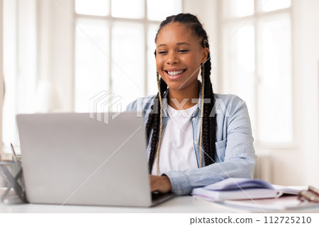 Joyful black female student engaged in e-learning on laptop at home Joyful black female student engaged in e-learning on laptop at home 112725210