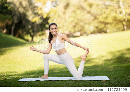 A serene woman in a white yoga outfit maintains a balanced yoga pose with grace and focus A serene woman in a white yoga outfit maintains a balanced yoga pose with grace and focus 112725499