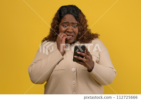 Shocked chubby african american woman looking at smartphone screen Shocked chubby african american woman looking at smartphone screen 112725666