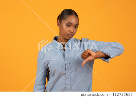 Young black woman expresses discontent giving thumbs down in studio 112725695