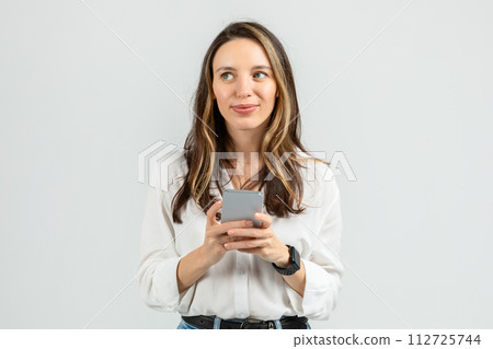 Contemplative young woman in a white blouse holding a smartphone Contemplative young woman in a white blouse holding a smartphone 112725744