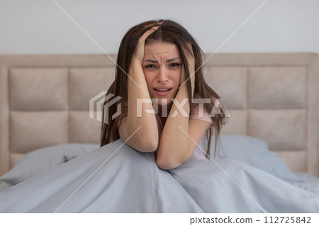 Stressed woman in bed with hands on head, looking distressed 112725842