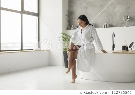 Cheerful Young Indian Woman In Bathrobe Touching Smooth Legs 112725845
