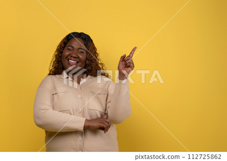 Cheerful overweight black lady pointing at blank space Cheerful overweight black lady pointing at blank space 112725862
