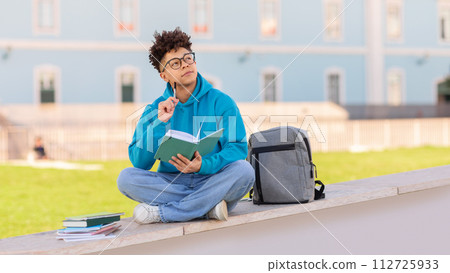 student guy studies writing in workbook with pensive expression outdoors student guy studies writing in workbook with pensive expression outdoors 112725933