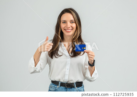Cheerful young woman giving a thumbs up while holding a blue credit card with a contactless payment symbol Cheerful young woman giving a thumbs up while holding a blue credit card with a contactless payment symbol 112725935