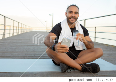 man rests at sea boardwalk holding smartphone and water bottle 112726052