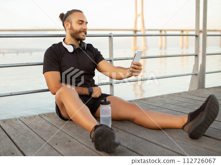 Sporty man with headphones checks fitness apps on phone outdoors 112726067