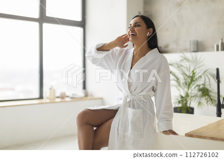 Young indian woman in bathrobe singing while filling bathtub Young indian woman in bathrobe singing while filling bathtub 112726102