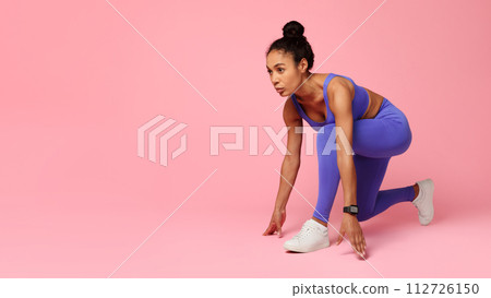 black woman in sporty attire crouches ready for running, studio 112726150
