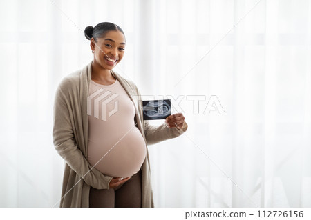 Cheerful young pregnant black woman showing baby sonogram 112726156