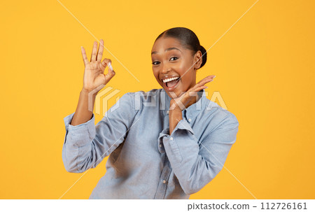 African American woman shows OK hand gesture over yellow backdrop 112726161
