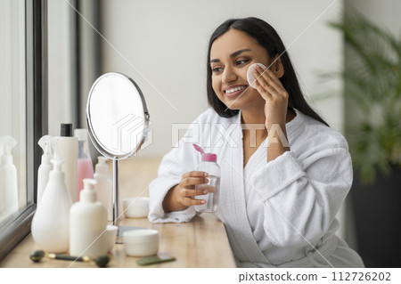 Positive young indian woman cleansing face in bathroom 112726202