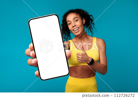 African lady in sportswear shows smartphone gives thumbs up, studio African lady in sportswear shows smartphone gives thumbs up, studio 112726272