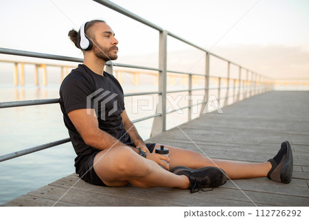 athlete guy in headphones sits by the pier relaxing outdoor athlete guy in headphones sits by the pier relaxing outdoor 112726292
