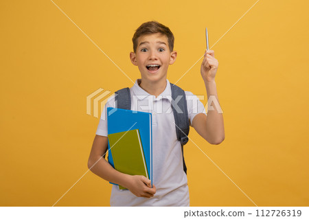 Idea Concept. Excited schoolboy with backpack and notebooks pointing upwards with pencil Idea Concept. Excited schoolboy with backpack and notebooks pointing upwards with pencil 112726319