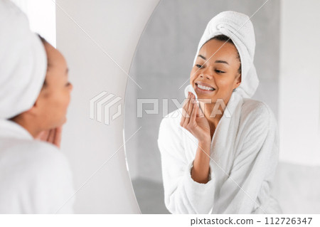 Black lady using cosmetic applying with cotton pad at bathroom Black lady using cosmetic applying with cotton pad at bathroom 112726347