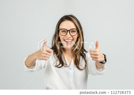 A smiling young woman with long hair and glasses gives two enthusiastic thumbs up A smiling young woman with long hair and glasses gives two enthusiastic thumbs up 112726373