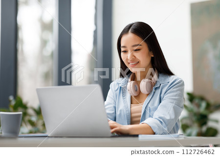 Smiling asian freelancer woman with headphones working on laptop 112726462