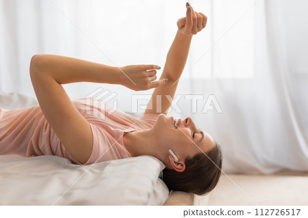 Happy woman lying in bed with earbuds, enjoying music 112726517