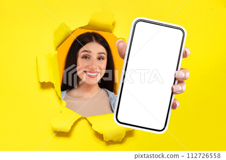 Smiling young woman with long hair peeking through a torn yellow backdrop Smiling young woman with long hair peeking through a torn yellow backdrop 112726558