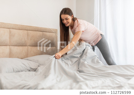 Happy woman making bed in daylight and smiling 112726599