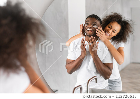 African American loving wife applies moisturizer to husband's skin indoors 112726615