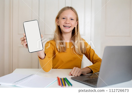 Educational App. Teen Girl Demonstrating Blank Smartphone, Sitting At Desk With Laptop 112726673