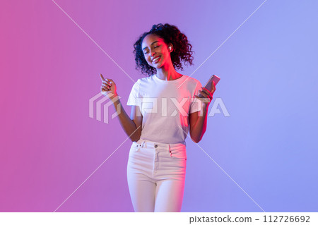 Happy lady with smartphone and earbuds enjoying music on colorful background Happy lady with smartphone and earbuds enjoying music on colorful background 112726692