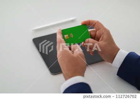 Close-up of a businessman's hands carefully examining a green bank card 112726702