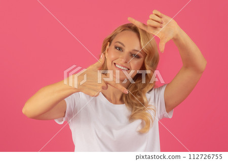 Blonde woman with cheerful smile making photo frame gesture, studio Blonde woman with cheerful smile making photo frame gesture, studio 112726755