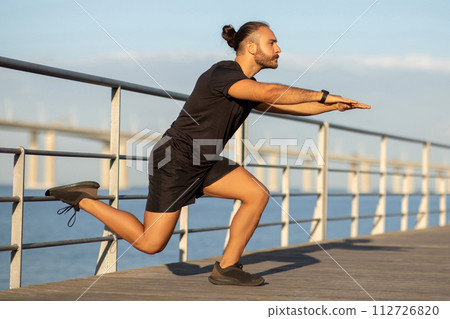 guy in activewear doing single leg lunge exercising at pier guy in activewear doing single leg lunge exercising at pier 112726820