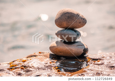 Balanced pebble pyramid on the beach on a sunny day. Abstract Sea bokeh on the background. Selective focus. Zen stones on the sea beach, meditation, spa, harmony, calmness, balance concept 112726849