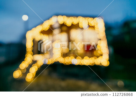 Abstract defocused bright Christmas lights on wooden house, creating decorative illumination in evening scene 112726868