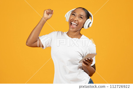 black woman in wireless headset with smartphone enjoys tunes, studio 112726922