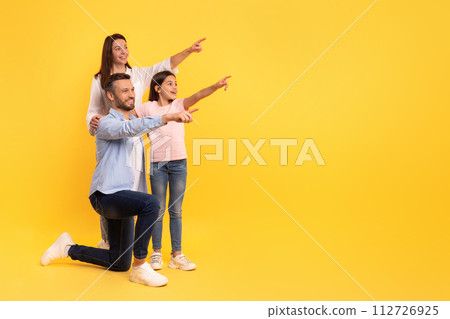 family of parents and daughter pointing at empty space, studio 112726925