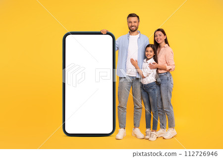 Parents and daughter leaning on phone mockup on yellow backdrop 112726946