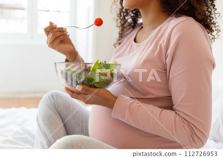 Closeup of black pregnant woman enjoying nutritious bowl of vegetable salad Closeup of black pregnant woman enjoying nutritious bowl of vegetable salad 112726953