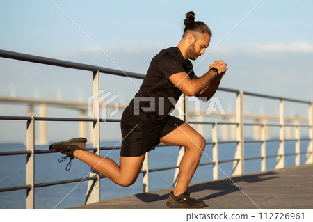 athlete guy doing single leg lunge training by the seaside athlete guy doing single leg lunge training by the seaside 112726961