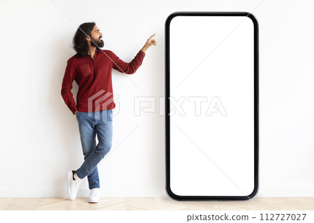 Curious hindu guy pointing at huge phone with blank screen Curious hindu guy pointing at huge phone with blank screen 112727027